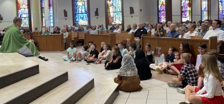 Children gather at the foot of the altar to listen to a priest's homily