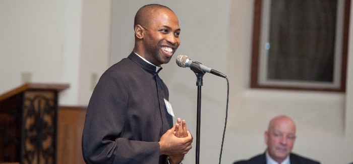 Fr. Nnamdi smiling and speaking into a microphone at an event