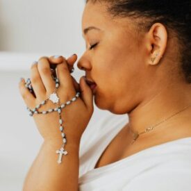 A woman praying the rosary with her eyes closed in prayer