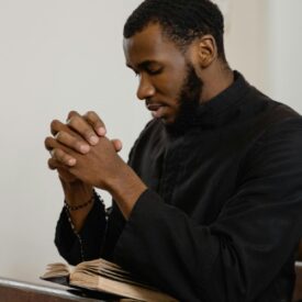 A man praying in a church pew with his hands folded and head bowed