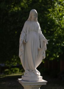 A white statue of mary stands in a garden