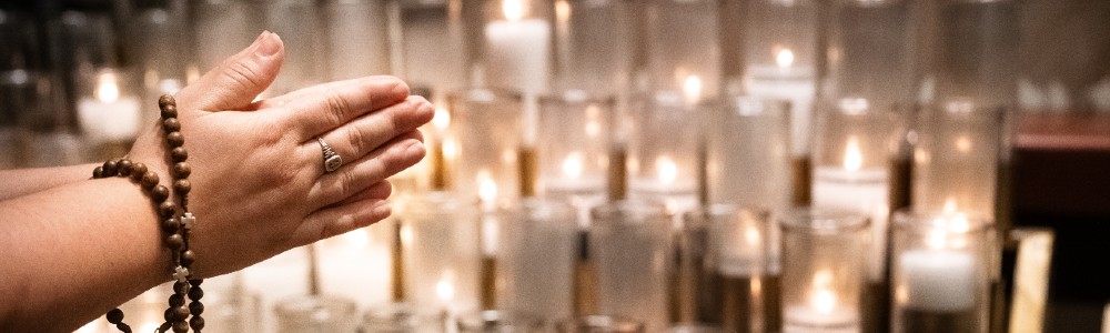 A woman's hands folded in prayer on All Souls Day in front of rows of lit candles