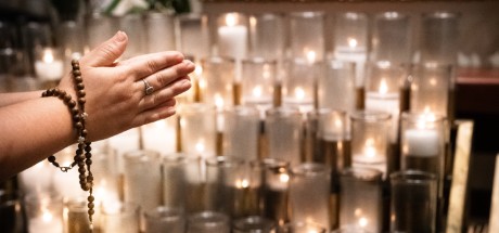 A woman's hands folded in prayer on All Souls Day in front of rows of lit candles