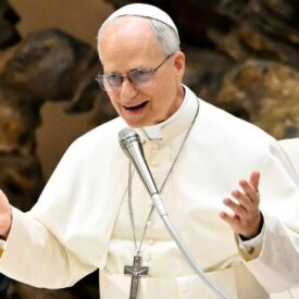 Pope Leo XIV speaks into a microphone with his hands open wide